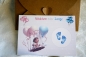Preview: Geschlecht verkünden - Rubbelkarte mit Umschlag aus Kraftpapier. Liebevoll gestaltete Karte in Größe A6 zeigt Baby auf einer Schaukel mit rosa und blauen Luftballons. Enthülltes Bild mit blauen Fußabdrücken für Junge. Perfekte Wahl für Gender-Reveal-Party