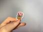 Preview: Kleiner Sticker mit handgezeichneten Blumen in rosa und orange, gehalten in der Hand.