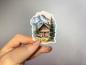 Preview: Sticker einer traditionellen Berghütte aus Holz in den Alpen, umgeben von Tannenbäumen und majestätischen Berggipfeln im Hintergrund.