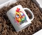Preview: Weißer Kaffeebecher mit buntem, lustigem Hühnerdesign und dem Text 'Coffee first', präsentiert in einer Geschenkbox mit Papierfüllmaterial. Perfektes Geschenk für humorvolle Kaffeeliebhaber.