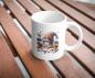 Preview: Weißer Kaffeebecher mit niedlichem Gnom-Design, umgeben von bunten Blumen und Bastelutensilien, auf einer Holzoberfläche. Perfektes Geschenk für kreative Seelen und Gartenliebhaber.