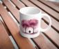 Preview: Weiße Tasse mit einem romantischen Aquarellmotiv eines Paares, das unter rosafarbenen Bäumen spaziert, auf einem Holztisch platziert. Ein zartes Design, ideal als Geschenk für besondere Anlässe oder als Erinnerung an romantische Momente.