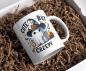 Preview: Weiße Tasse mit Halloween-Design eines niedlichen Geistes in Hexenhut, der neben einem Kürbis sitzt, mit dem Text ‚Cute but Creepy‘. Verziert mit einem Seil, Sternen und Fledermäusen – perfekt für Halloween-Fans, die sowohl süße als auch gruselige Motive