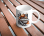 Preview: Keramiktasse mit herbstlichem Design und der Aufschrift 'Just a Girl Who Loves Books'. Die Illustration zeigt einen Kürbis, einen Stapel Bücher, ein herbstliches Getränk, einen karierten Schal und bunte Herbstblätter. Die Tasse steht auf einem Holztisch u