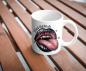 Preview: Weiße Tasse mit dem frechen Halloween-Design 'Bad Witch', das große, glänzende Lippen in Schwarz und Rosa mit herausgestreckter Zunge zeigt, umgeben von kleinen Fledermäusen und dem Schriftzug 'Bad Witch'. Die Tasse steht auf einer Holzoberfläche und hebt