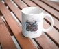 Preview: Weiße Keramiktasse mit kunstvoller Aquarell-Illustration einer Vintage-Schreibmaschine, verziert mit floralen Elementen und einem personalisierten Namen „Claudia“. Die Tasse steht auf einem Holztisch in natürlichem Licht und vermittelt eine gemütliche, in
