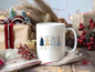 Preview: Weiße Weihnachtstasse mit blau-goldenem Weihnachtsbaum-Design, präsentiert in einem festlichen Setup mit Geschenken, Lichtern und winterlicher Dekoration.