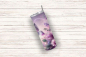 Preview: Ein eleganter Thermobecher mit einem Design aus violetten Schmetterlingen und großen Blumen liegt schräg auf einer weißen Holzoberfläche. Das detailreiche florale Muster und die zarten Schmetterlinge in verschiedenen Lila- und Rosatönen verleihen dem Bech