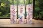 Preview: Drei personalisierte Thermobecher mit dem Namen „Ella“, gestaltet in einem romantischen Schmetterlings- und Blumen-Design auf einem pastellfarbenen Hintergrund. Die Becher stehen auf einer Holzoberfläche mit einem Wald im Hintergrund, was das träumerische