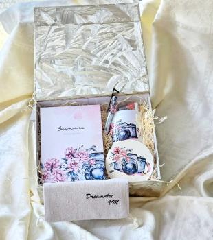 Handgefertigtes Fotografie-Geschenkset in einer dekorativen Box. Enthält ein personalisiertes Notizbuch mit dem Namen 'Susanne', einen runden Untersetzer mit einer Kamera-Illustration und Blumenmotiv, einen Kugelschreiber sowie einen kleinen Stoffbeutel m