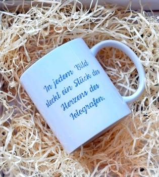 Handgefertigte weiße Tasse mit dem Schriftzug 'In jedem Bild steckt ein Stück des Herzens des Fotografen'. Präsentiert in einer dekorativen Holzwolle-Verpackung.