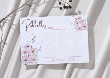 Personalisierte Rubbelkarte mit dem Namen „Steffi“ im zarten Blütendesign in Rosa. Die Karte liegt auf weichem, hellem Stoff mit Zweigen im Hintergrund. Sechs leere Rubbelfelder sind sichtbar.