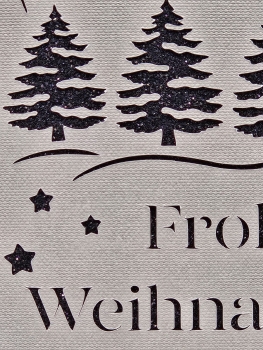 Detailansicht einer handgefertigten Weihnachtskarte in Grau mit schwarzem Glitzerhintergrund. Nahaufnahme zeigt glitzernde Weihnachtsbäume, filigran geschnittene Sterne und den Schriftzug 'Frohe Weihnachten'.