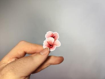 Hand, die einen Blumenaufkleber mit einer zarten rosa Blüte hält, gestaltet von DreamArt VM.