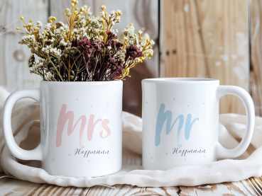 Zwei personalisierte Tassen mit den Aufschriften „Mrs Hoffmann“ in Rosa und „Mr Hoffmann“ in Hellblau, verziert mit feinen Punkten. Romantisches Geschenk für Paare, zur Hochzeit oder zum Valentinstag.