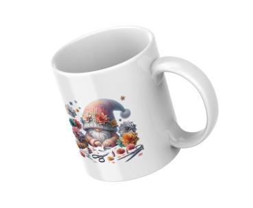 Weißer Kaffeebecher mit niedlichem Gnom-Design, umgeben von bunten Blumen und Bastelutensilien, in schräger Position. Perfekt für kreative Seelen und Gartenliebhaber als Geschenk.
