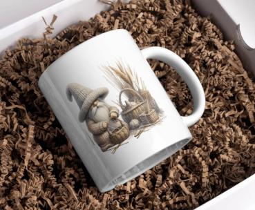 Weiße Tasse mit einem Motiv eines freundlichen Gnoms in einer großen gestrickten Mütze. Der Gnom hält einen Korb in den Händen und ist umgeben von weiteren Körben sowie Weizenhalmen. Perfekt für Liebhaber von ländlichem und rustikalem Design.