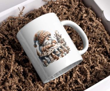 Weiße Tasse mit einer Illustration eines kleinen Wichtels in einem großen, gestrickten Hut und Pullover, der an einem Tisch voller kleiner Figuren sitzt. Der Wichtel scheint die Figuren zu bemalen, umgeben von Pinseln und Farbeimern. Ein Design, das handw