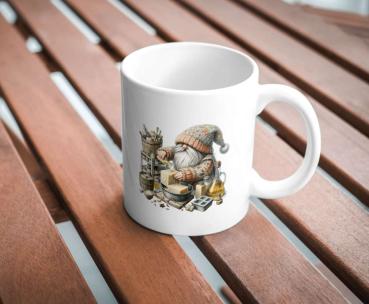 Weißer Keramikbecher mit einem Motiv eines Gnoms in Strickkleidung, der handgemachte Seifen herstellt. Der Becher steht auf einem Holztisch und ist perfekt für Liebhaber von Handwerkskunst und Kreativität.