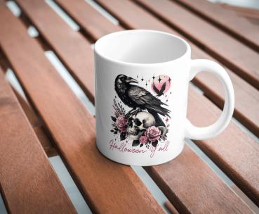 Weiße Keramiktasse mit Halloween-Motiv: Ein schwarzer Rabe sitzt auf einem Totenschädel, umgeben von rosafarbenen Rosen. Im Hintergrund ist ein rosa Mond mit einem fliegenden Raben zu sehen. Der Schriftzug 'Halloween y'all' verleiht dem Design einen festl