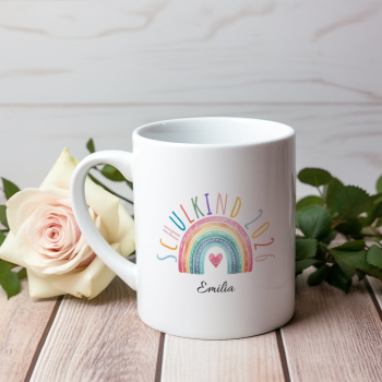 Preview: Personalisierte Tasse „Schulkind 2026“ – Motiv B mit großem buntem Regenbogen, Herzsymbol und gebogenem Schriftzug, Name „Emilia“, auf Holztisch mit Rosen im Hintergrund fotografiert.
