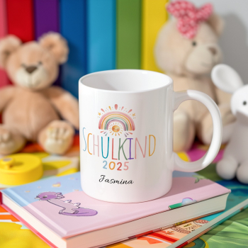 Personalisierte Tasse „Schulkind 2025“ mit Regenbogen und Sonnengesicht, Name „Jasmina“, arrangiert auf Kinderbuch, im Hintergrund bunte Spielsachen und Teddys.