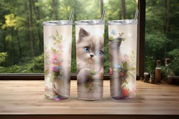 Drei Thermobecher mit einem niedlichen Design, das ein flauschiges Kätzchen mit großen blauen Augen in einem Korb zeigt, umgeben von bunten Blumen und grünen Blättern. Die Becher stehen auf einer Holzoberfläche mit einem Waldhintergrund, was eine frische,