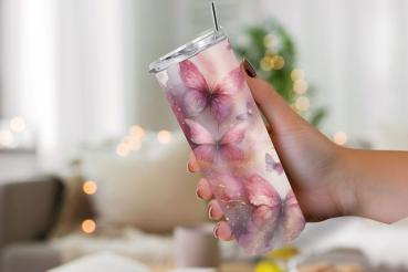 Eine Hand hält einen Thermobecher mit einem zarten rosa Schmetterlingsdesign. Der Becher zeigt verschiedene rosa Schmetterlinge auf einem pastellfarbenen, wolkigen Hintergrund, verziert mit subtilen goldenen Akzenten. Im Hintergrund ist eine unscharfe, ge