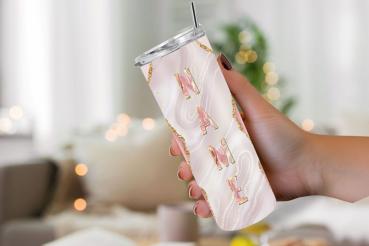 Hand hält einen eleganten Thermobecher mit personalisiertem Design. Der Becher hat einen cremefarbenen Hintergrund mit goldenen Glitzerakzenten und den Schriftzug 'NAME' in großen, roségoldenen Buchstaben. Im Hintergrund ist eine unscharfe, gemütliche Woh