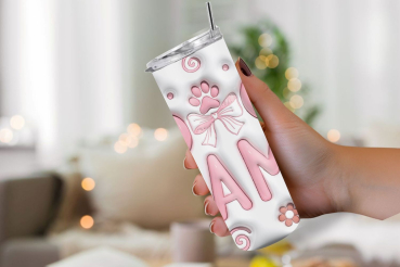 Hand hält einen weißen Thermobecher mit der Aufschrift 'DOG MAMA' in rosa Buchstaben. Der Becher ist mit einem Pfotenabdruck, einer Schleife und Blumenmotiven verziert. Hintergrund zeigt ein gemütliches Wohnzimmer mit unscharfen Lichtern. Perfektes Gesche