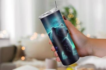Hand hält einen schlanken Reisebecher mit einem Bärenmotiv, das in leuchtendem Blau und Grün dargestellt ist. Der Bär zeigt Sternbilder und den Nachthimmel mit Polarlichtern. Der Becher hat einen durchsichtigen Deckel und einen Edelstahlstrohhalm, ideal f