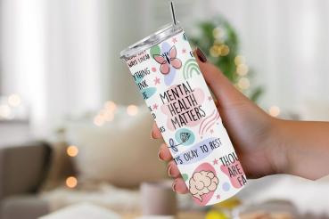 Hand hält einen weißen Thermobecher mit der Aufschrift 'Mental Health Matters' und weiteren positiven Botschaften zur psychischen Gesundheit wie 'It's okay to rest'. Der Becher ist mit Illustrationen von Schmetterlingen, Pflanzen und Gehirnen in beruhigen