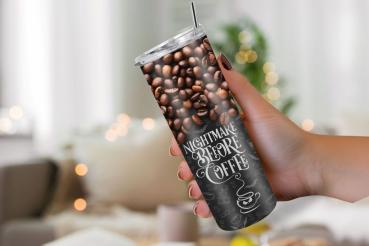 Hand hält einen Thermobecher mit einem Design aus Kaffeebohnen im oberen Bereich und schwarzem Hintergrund im unteren Bereich, dekoriert mit kleinen Kaffeesymbolen und dem Schriftzug 'Nightmare Before Coffee'. Der Hintergrund zeigt einen gemütlichen, sanf