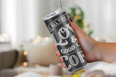 Person hält einen schwarzen Thermobecher mit weißem Kreideschriftzug 'All you need is love & a good cup of coffee', im Retro-Tafelstil gestaltet.