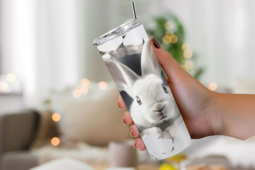 Hand hält einen Thermobecher mit einem Design, auf dem ein weißes Kaninchen aus einem realistisch wirkenden Riss in der Becheroberfläche hervorschaut. Der Hintergrund des Designs ist hell und minimalistisch, was das Kaninchen und die gebrochenen Wandeffek