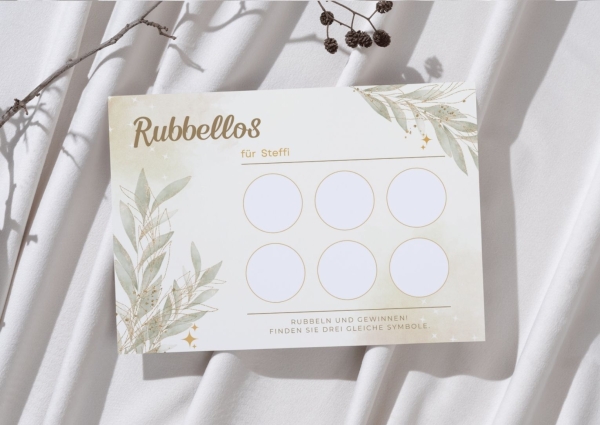 Personalisierte Rubbellos-Karte mit dem Namen „Steffi“ im eleganten Boho-Gold-Design mit zarten Blättern und goldenen Akzenten. Die Karte liegt auf weichem, hellem Stoff mit dekorativem Zweig. Sechs leere Rubbelfelder sind sichtbar.