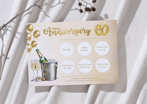 Freigerubbelte Jubiläums-Rubbelkarte mit goldener Aufschrift „Happy Anniversary“ und der Zahl 60. Zu sehen sind sechs Felder mit Begriffen wie „Massage“, „Kaffee im Bett“ und dreimal „Wellnesstag für zwei“ als Gewinn. Die Karte liegt auf weichem, weißem S