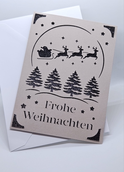 Handgefertigte Weihnachtskarte in Grau mit schwarzem Glitzerhintergrund. Filigranes Design zeigt den Weihnachtsmann im Schlitten, gezogen von Rentieren, sowie Weihnachtsbäume und Sterne. Karte wird mit einem passenden weißen Umschlag geliefert.
