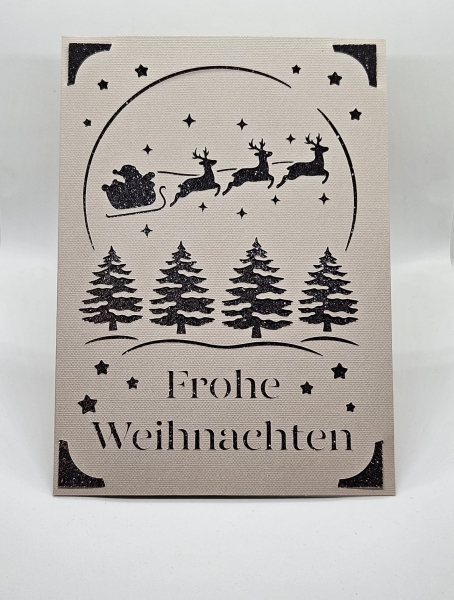 Vorderansicht einer handgefertigten Weihnachtskarte in Grau mit schwarzem Glitzerhintergrund. Filigranes Design zeigt Weihnachtsbäume, Sterne und den Schlitten des Weihnachtsmanns, gezogen von Rentieren. Der Schriftzug 'Frohe Weihnachten' ist kunstvoll au