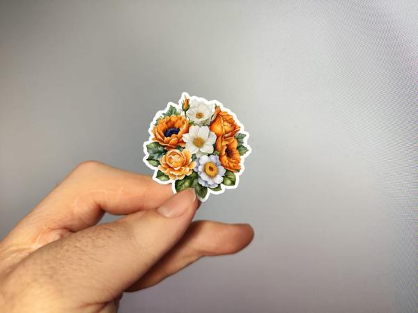 Hand, die einen Blumenaufkleber mit orangefarbenen und weißen Blüten hält, gestaltet von DreamArt VM.