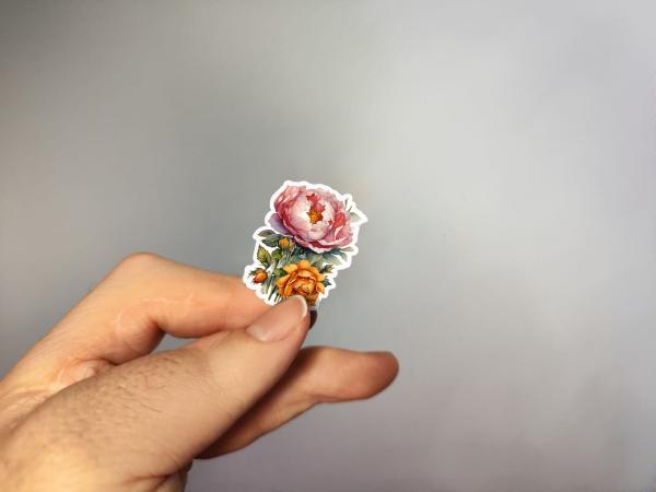 Kleiner Sticker mit handgezeichneten Blumen in rosa und orange, gehalten in der Hand.
