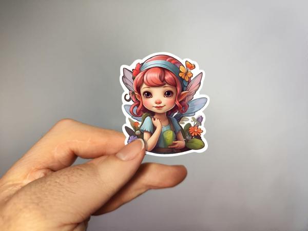 Hand, die einen Aufkleber einer süßen Fee mit rosa Haaren und Schmetterlingen hält, gestaltet von DreamArt VM.