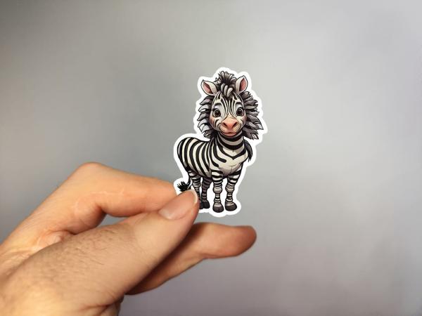 Hand, die einen Aufkleber in Form eines niedlichen Zebras hält, gestaltet von DreamArt VM.