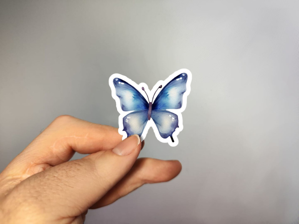 Hand, die einen Aufkleber in Form eines blauen Schmetterlings hält, gestaltet von DreamArt VM.