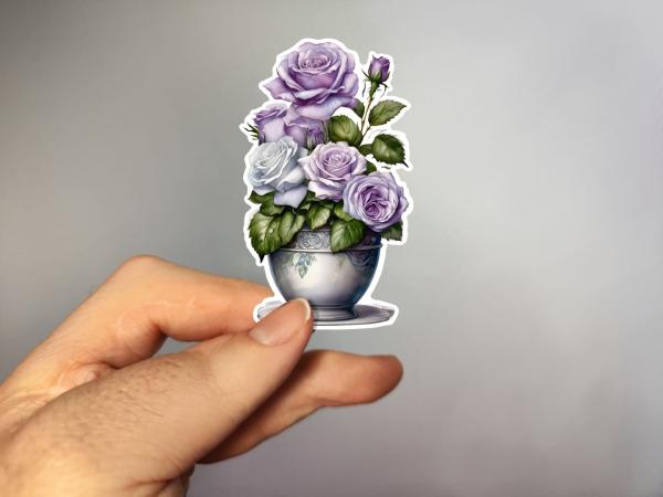 Aufkleber einer Blumenvase mit lila und weißen Rosen, umgeben von grünen Blättern. Ideal zur Dekoration und für kreative Projekte.