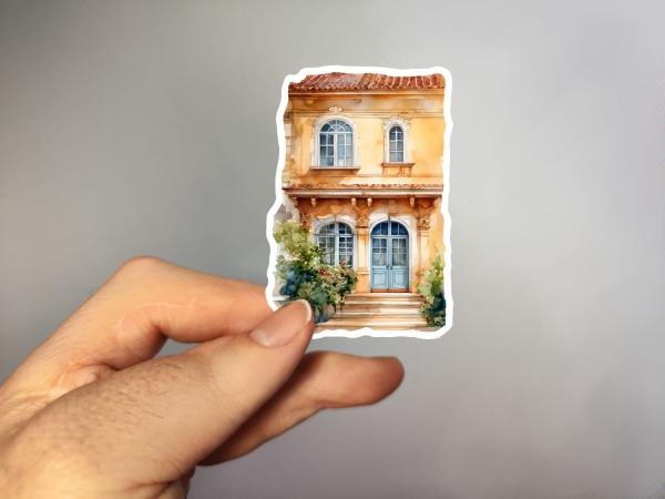 Aufkleber einer mediterranen Villa mit orangefarbener Fassade, blauen Doppeltüren und einem kleinen Balkon im ersten Stock. Bild A.