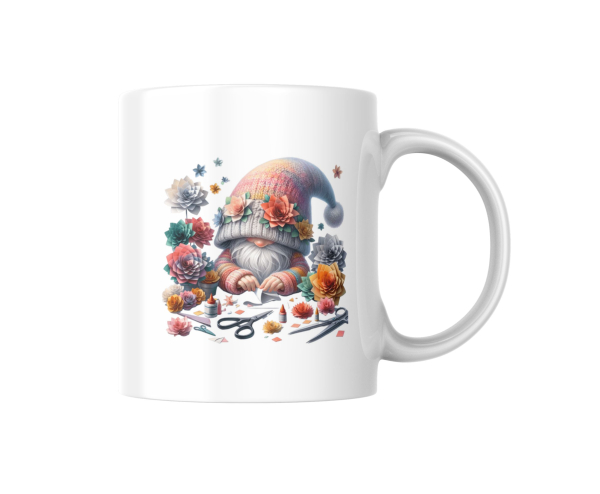 Weißer Kaffeebecher mit einem niedlichen Gnom-Design, umgeben von bunten Blumen und Bastelutensilien. Perfekt für kreative Menschen und Gartenliebhaber als Geschenkidee.