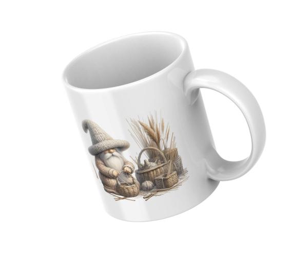 Weiße Tasse mit einem Motiv eines kleinen, strickenden Wichtels in einem großen Strickhut, der neben Körben und Bündeln von Weizen sitzt. Eine Illustration, die die Gemütlichkeit und das Landleben symbolisiert.