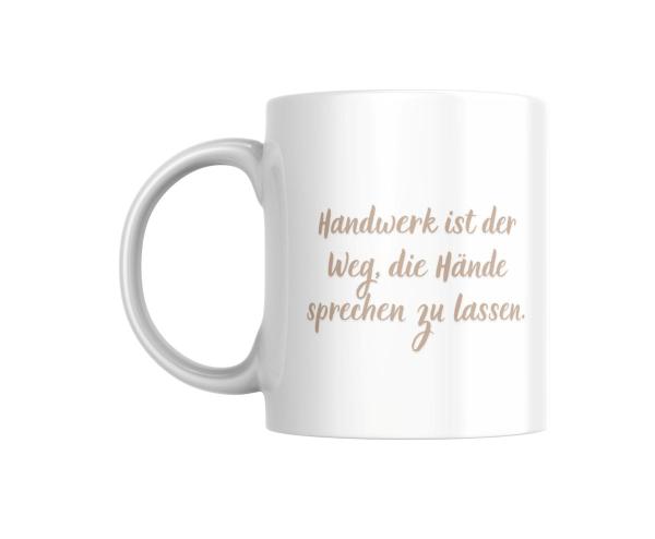 Weiße Tasse mit einem handgeschriebenen Spruch in beiger Farbe: ‚Handwerk ist der Weg, die Hände sprechen zu lassen.‘ Ein minimalistisches Design, das die Bedeutung des Handwerks und der Handarbeit hervorhebt.