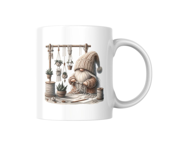 Ein weißer Keramikbecher ist auf einem weißen Hintergrund platziert. Der Becher zeigt eine lebendige Illustration eines Zwergs, der kreativ mit Makramee arbeitet. Die Detailgenauigkeit der Abbildung bringt die Freude am Handwerk zur Geltung.